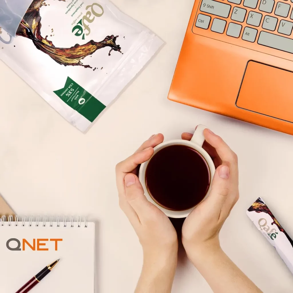 New Year, New Me? Here Are 6 Ways To Reset Your Health And Wellness In 2026 With Qnet 4 holding a cup of QAFE coffee next to laptop