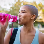 Girl hydrating in the garden post-workout, while another girl beams with happiness