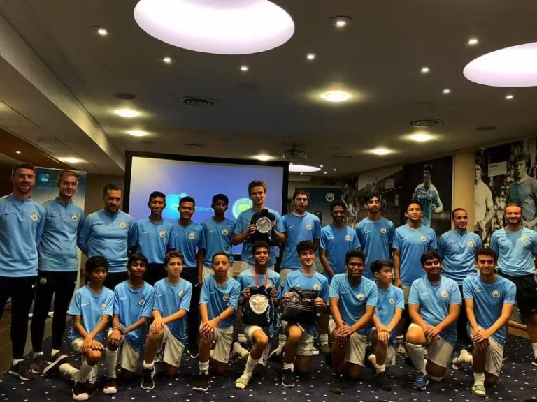 Kids from Indonesia in Man City Etihad Campus locker room posing with coaches and players. 